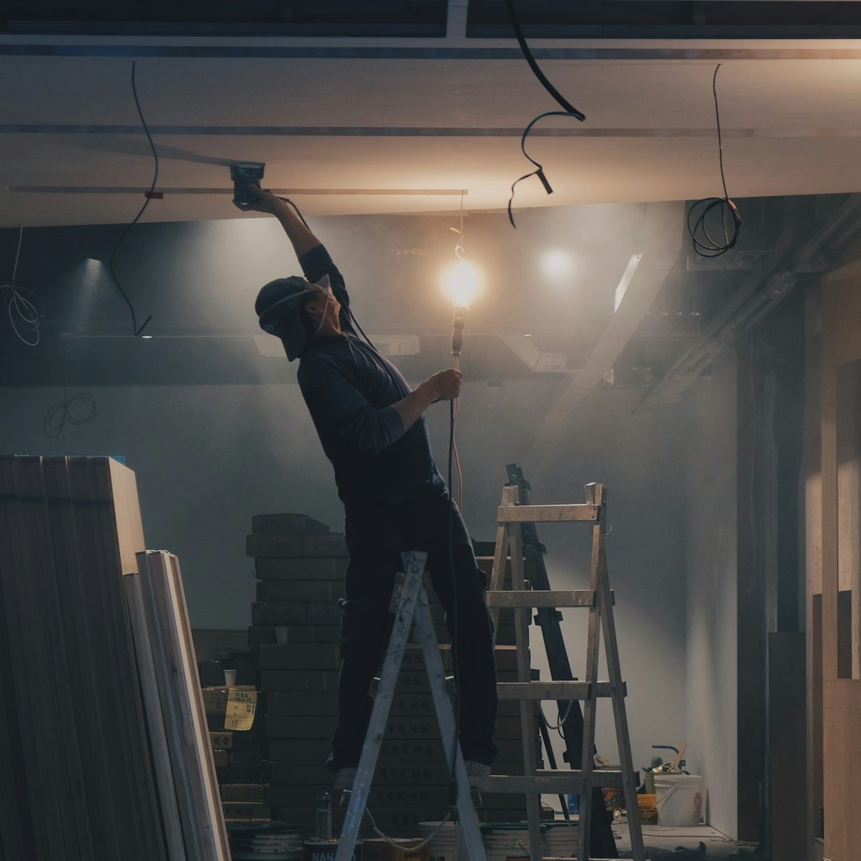 Arbeiter auf einer Leiter, der eine Decke mit einer Lampe bearbeitet.