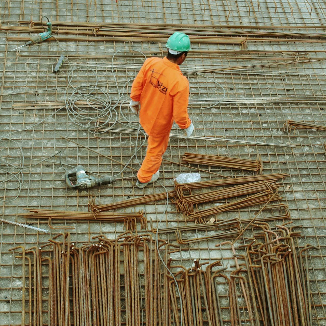 Arbeiter in orangefarbener Kleidung auf einer Baustelle zwischen Stahlstäben.